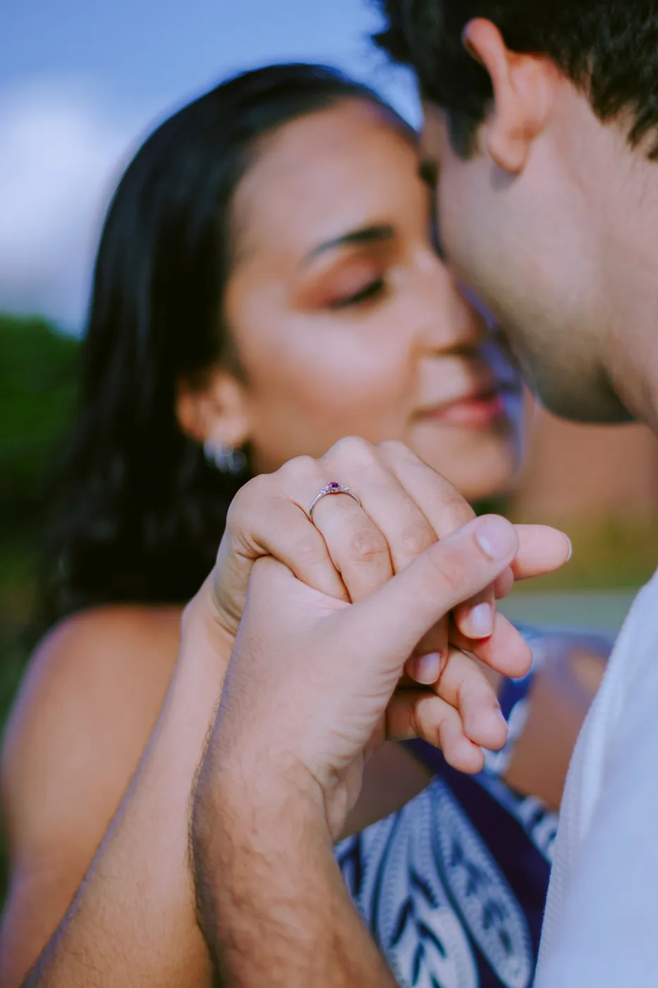 Pareja tomada de la mano mientras uno le besa los dedos bajo una luz cálida