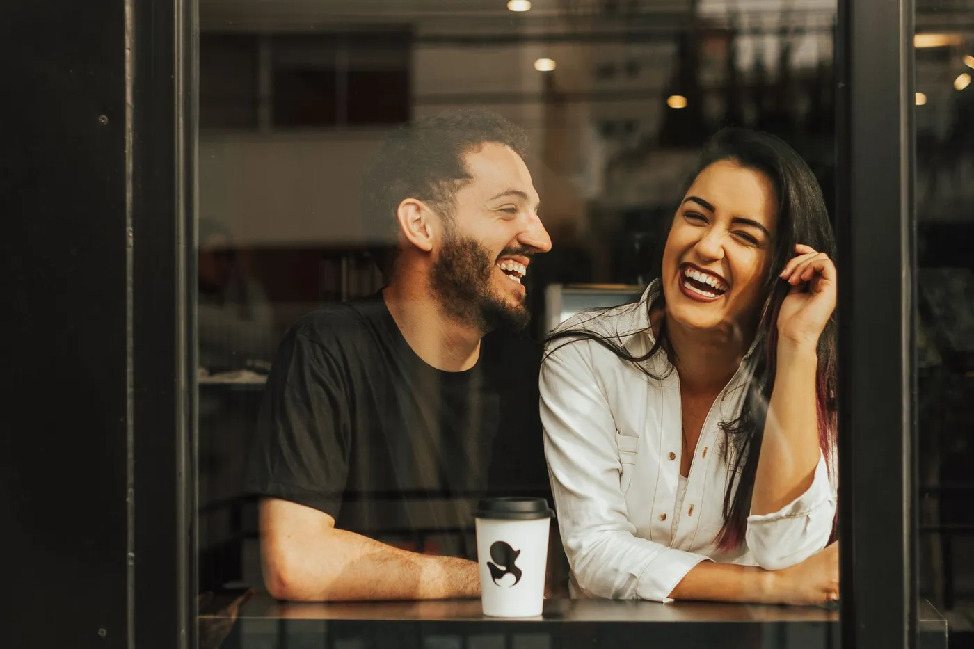 Pareja joven riendo juntos en una cafetería con un café sobre la mesa