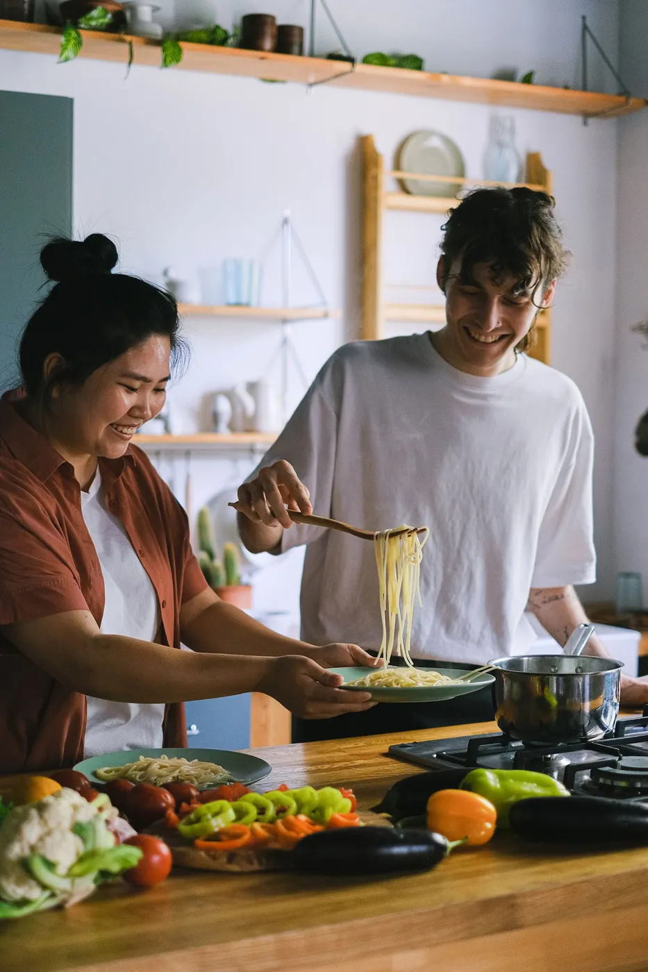 Pareja cocinando pasta juntos y riendo en la cocina