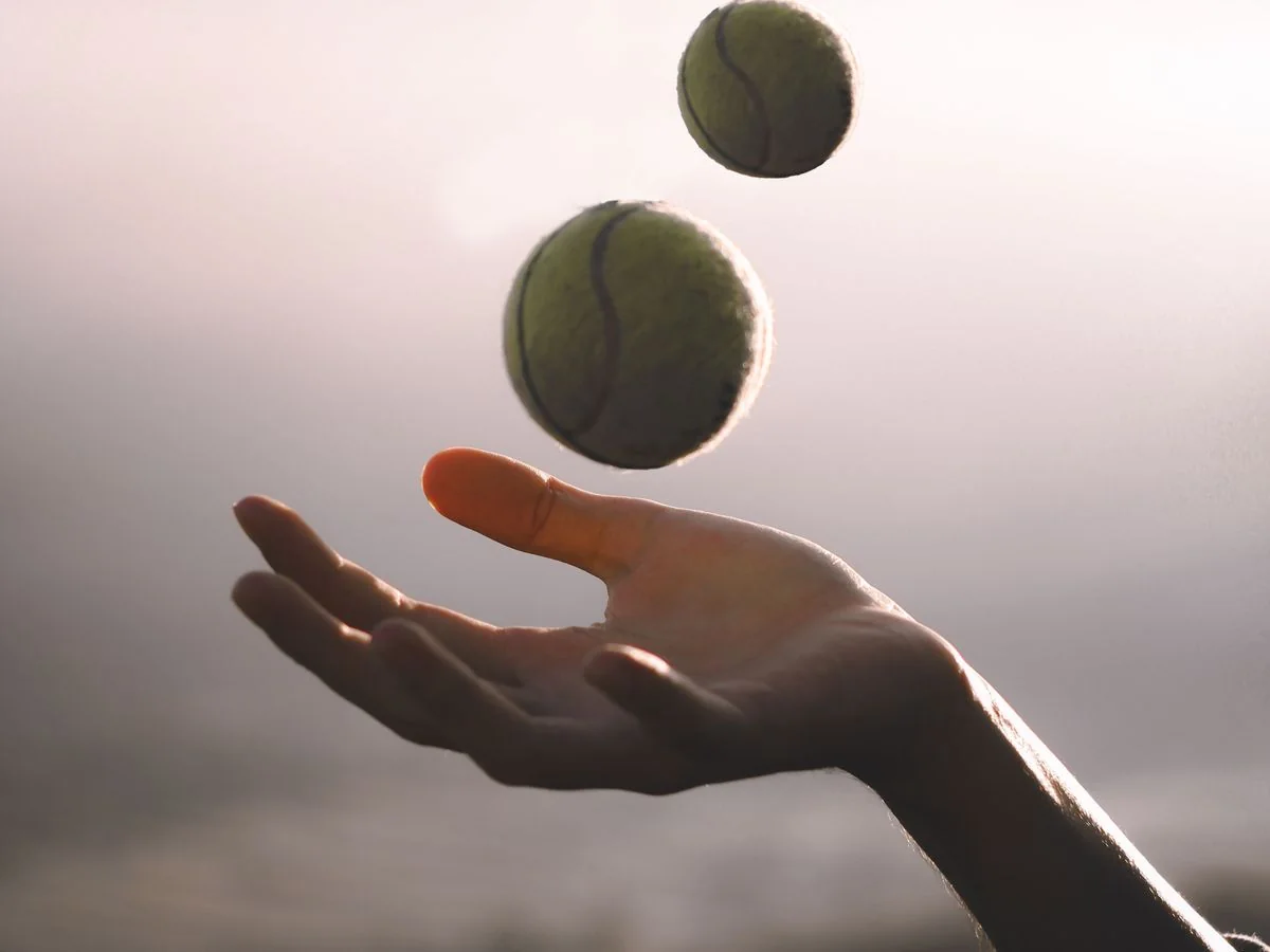 Una mano lanza pelotas de tenis al aire, a contraluz