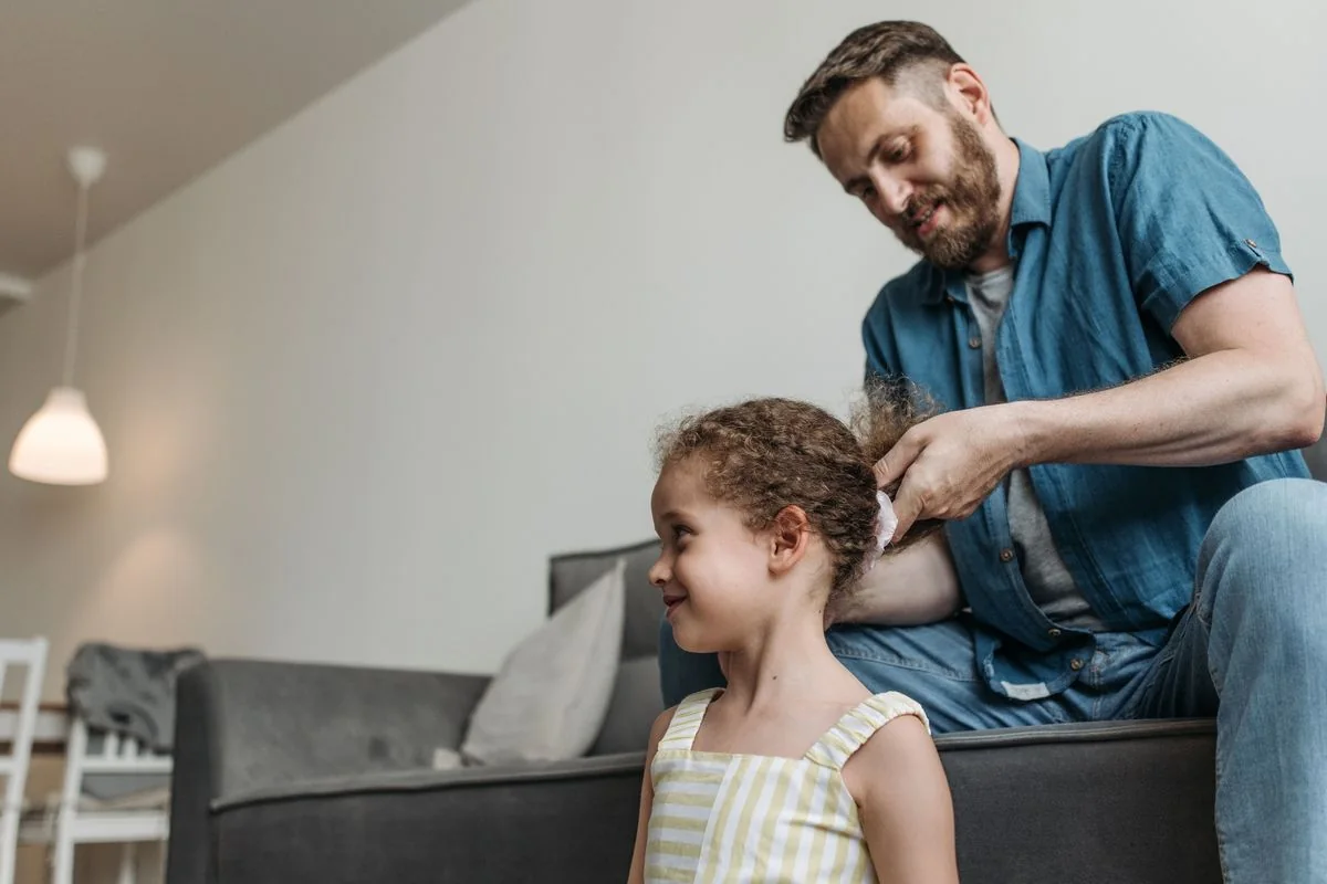Padre peinando a su hija en la sala; los dos sonríen