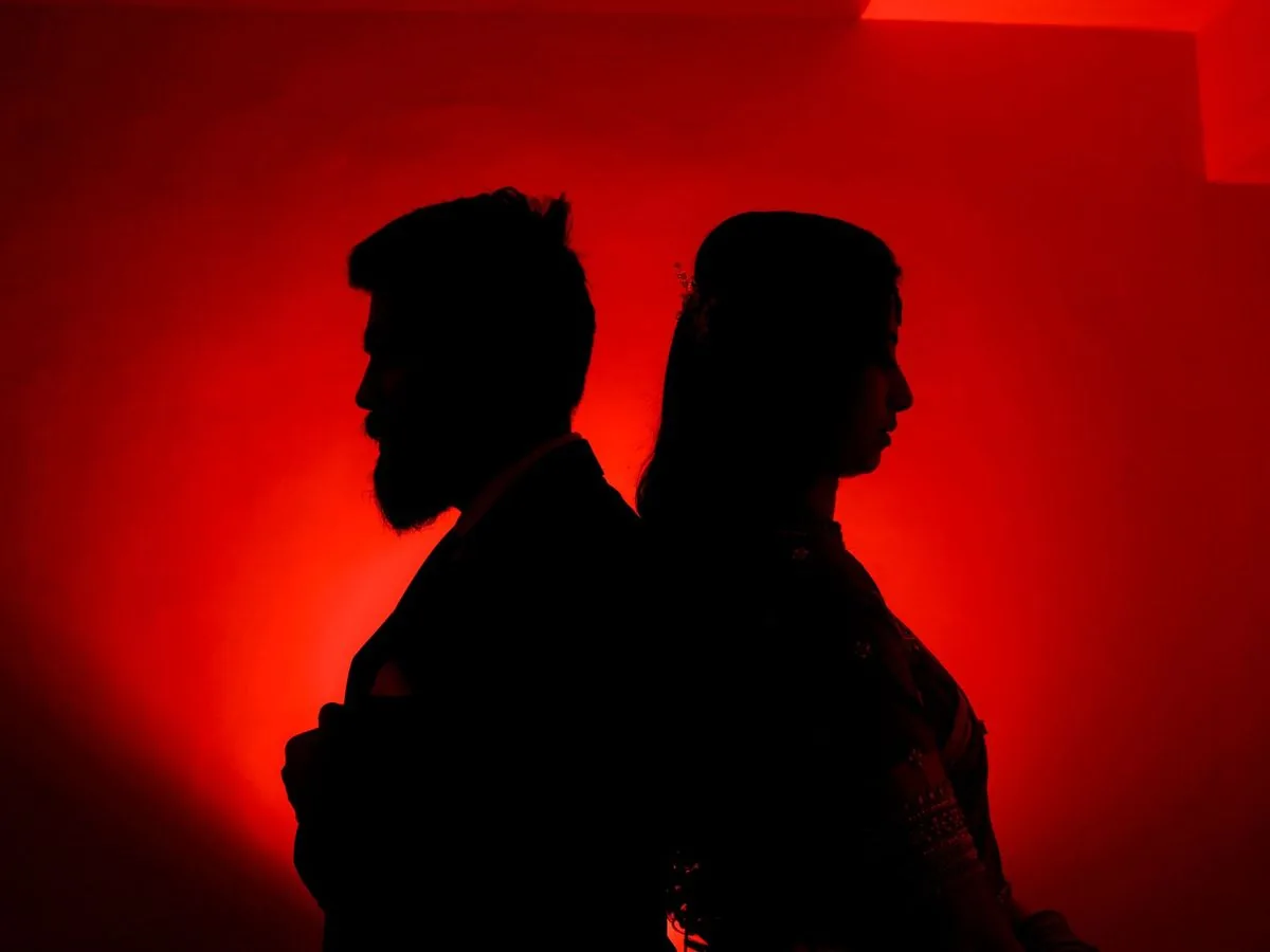 Siluetas de una pareja de espaldas, una contra la otra, sobre un fondo rojo