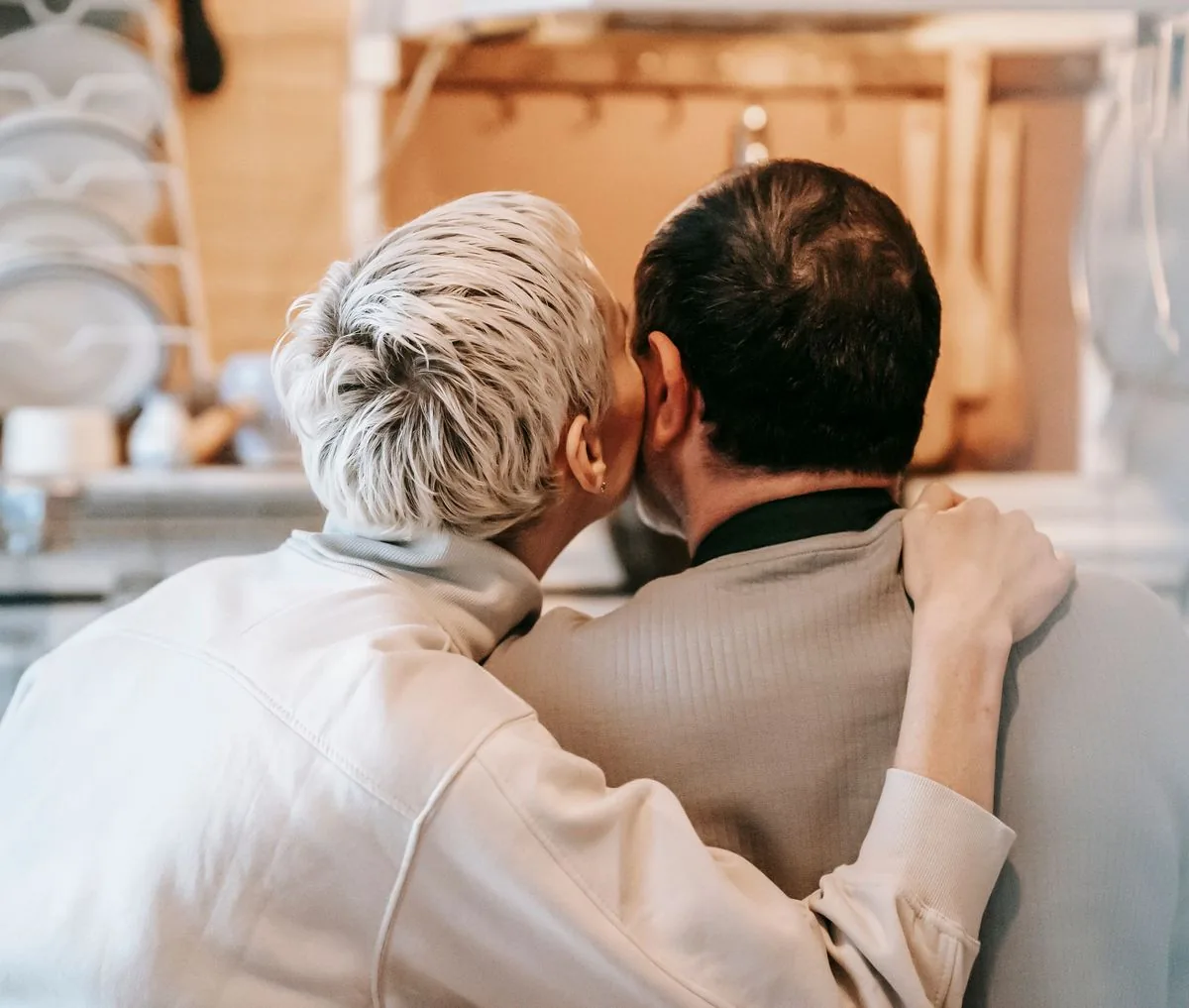 Pareja madura abrazándose en la cocina mientras ella le da un beso en la mejilla