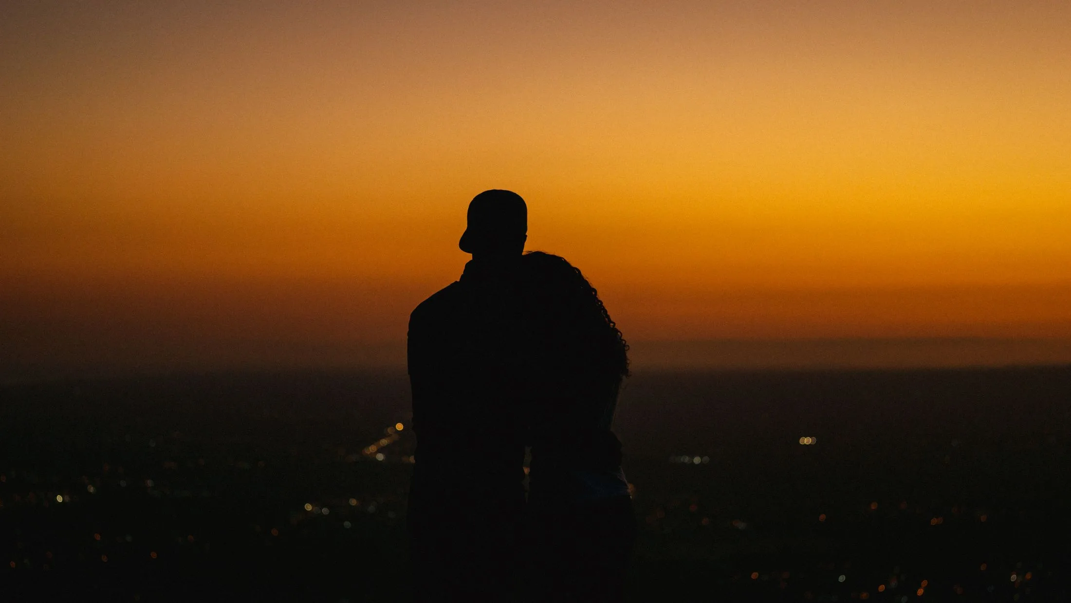 Pareja en silueta, cabeza con cabeza, frente a un atardecer sobre la ciudad