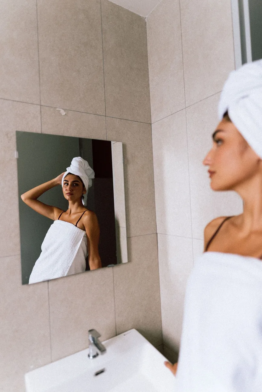 Mujer mirándose al espejo del baño, pensativa