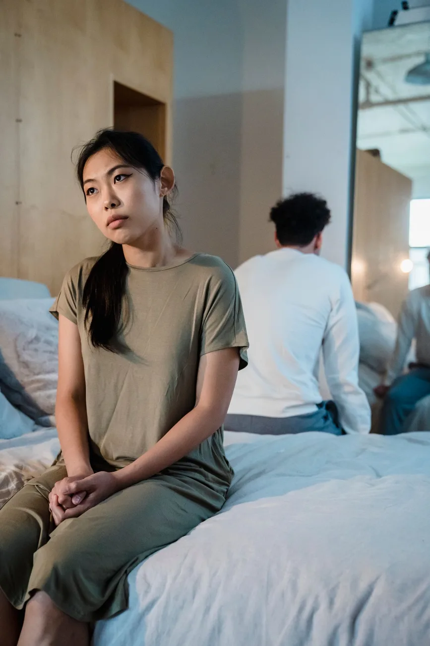 Pareja distante sentada en la cama, dándose la espalda