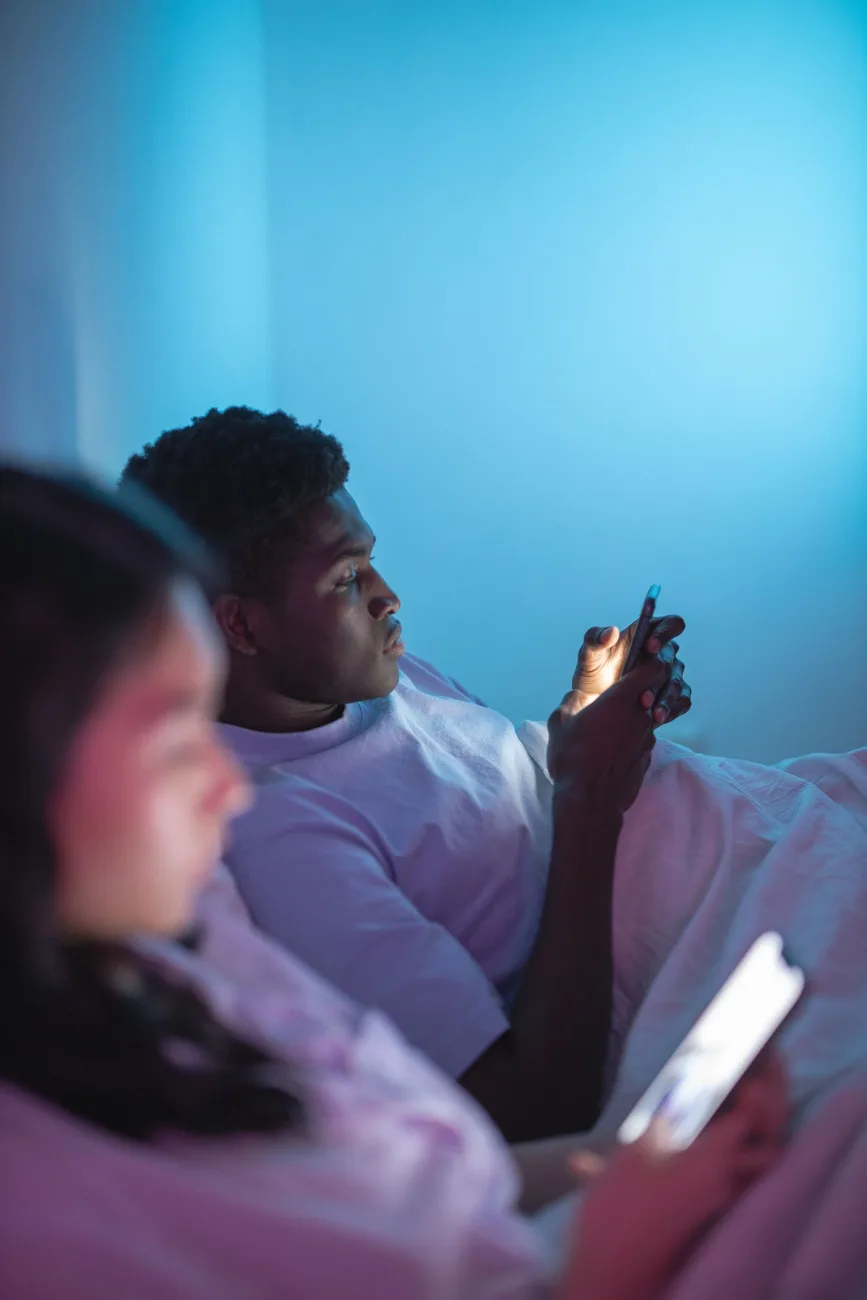 Pareja en la cama, cada uno absorto en su teléfono