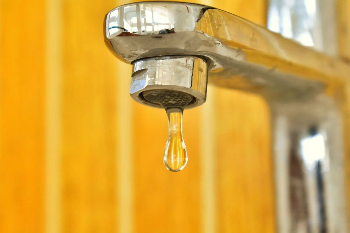 Una gota de agua a punto de caer de un grifo, sobre un fondo dorado