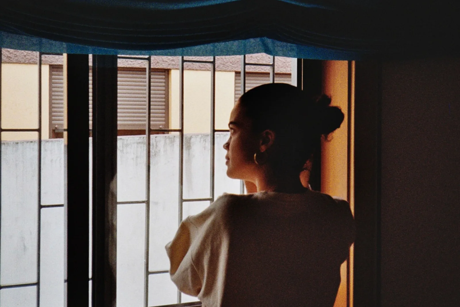Mujer de espaldas junto a una ventana con rejas, mirando hacia afuera en silencio