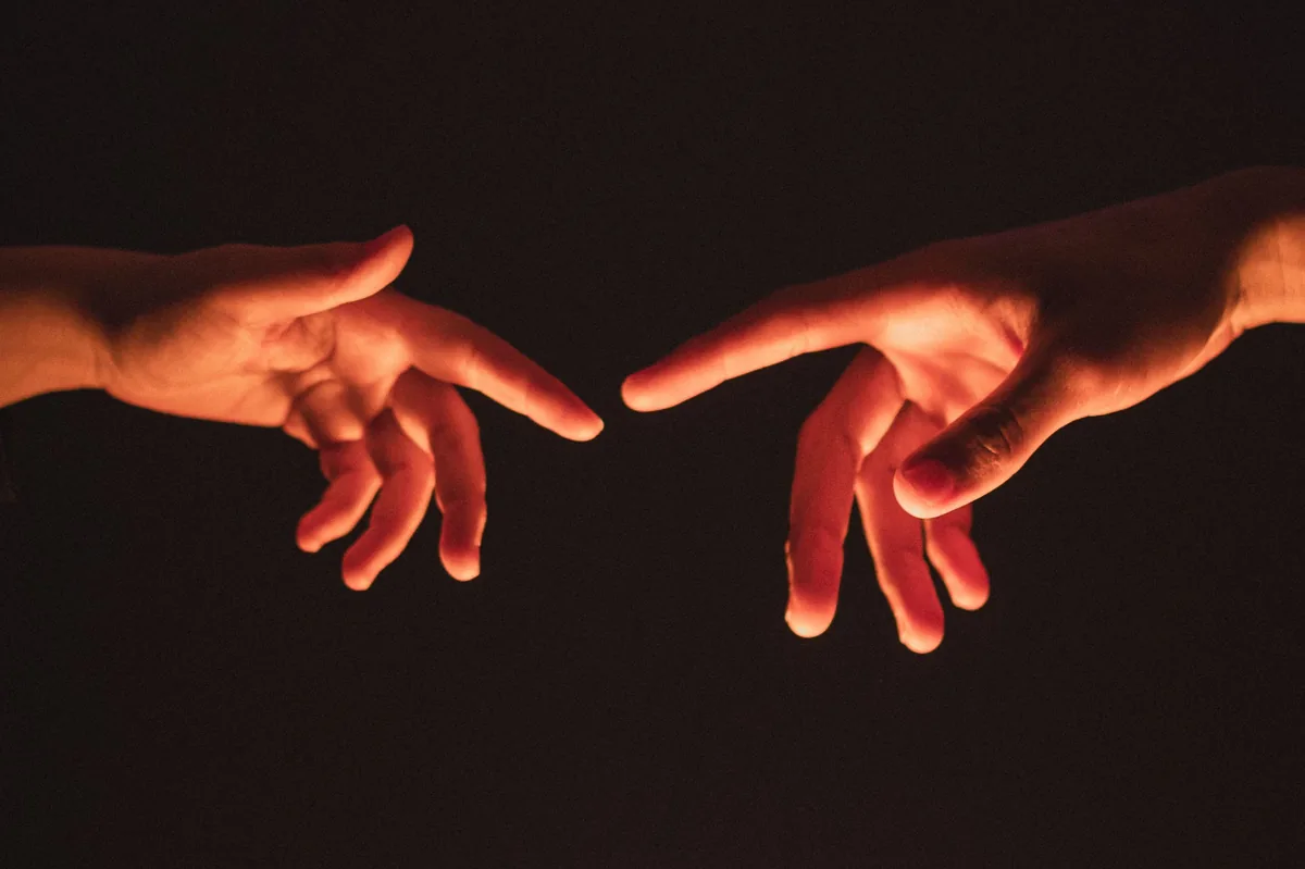Dos manos que se buscan en la oscuridad, iluminadas por una luz cálida