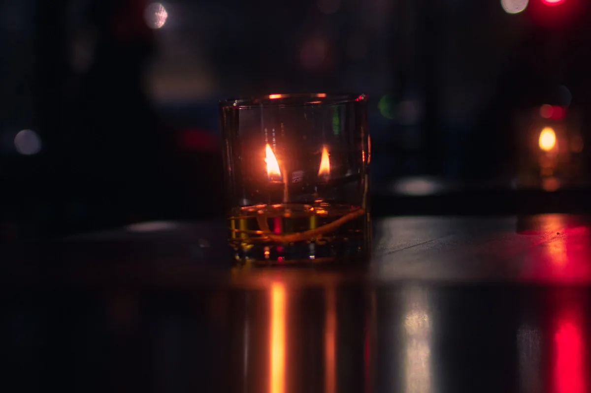 Una vela encendida dentro de un vaso, sobre una mesa oscura