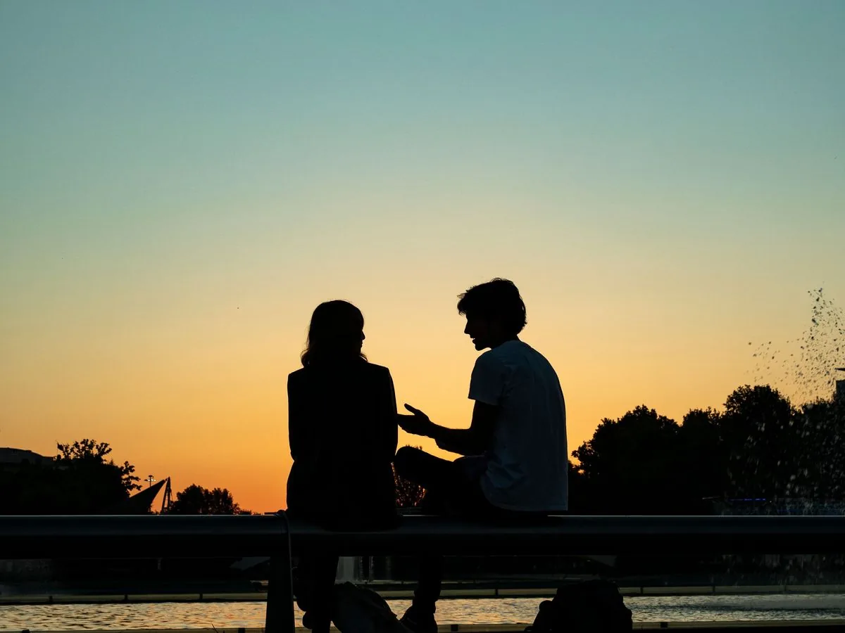 Silueta de una pareja sentada en una banca al atardecer: él habla con las manos y ella lo escucha