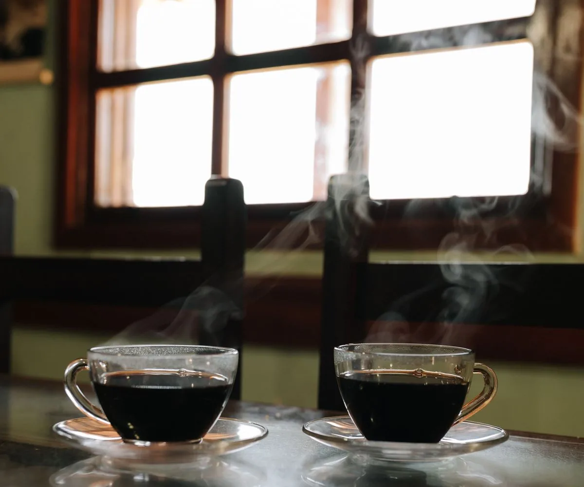 Dos tazas de café humeantes frente a una ventana iluminada