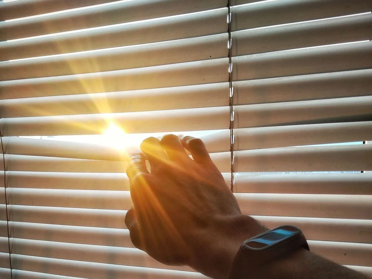 Una mano abre las persianas y deja entrar un rayo de sol dorado