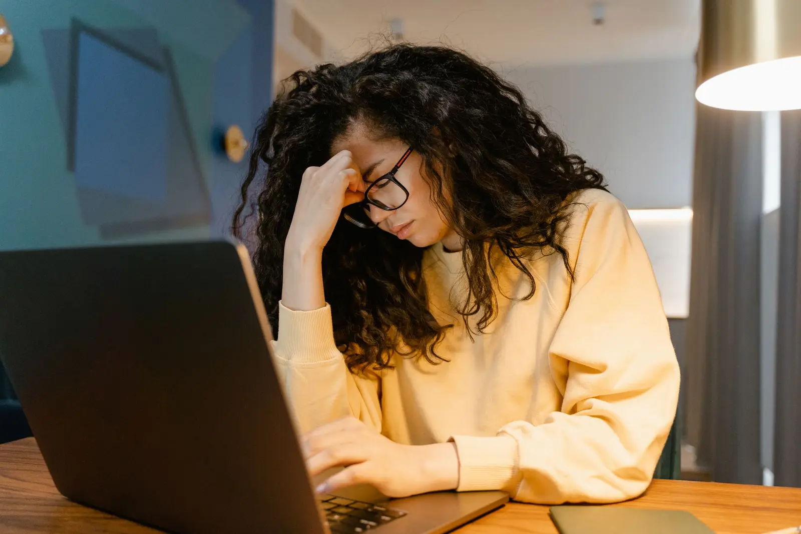 Mujer agotada frente a su laptop, de noche, con la mano en la frente
