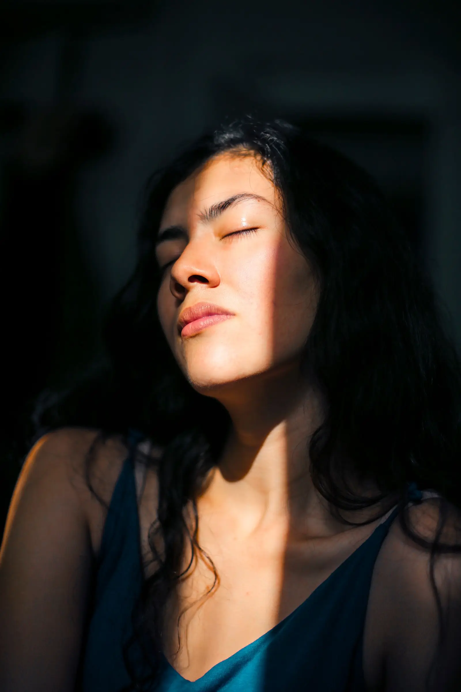 Rostro de una mujer con los ojos cerrados, iluminado por un rayo de sol en la penumbra