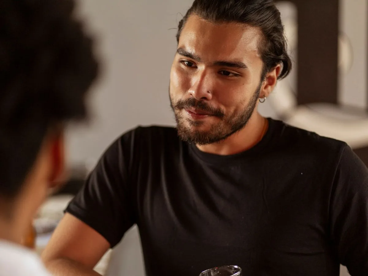Hombre con barba escuchando con atención y una leve sonrisa, en una luz cálida