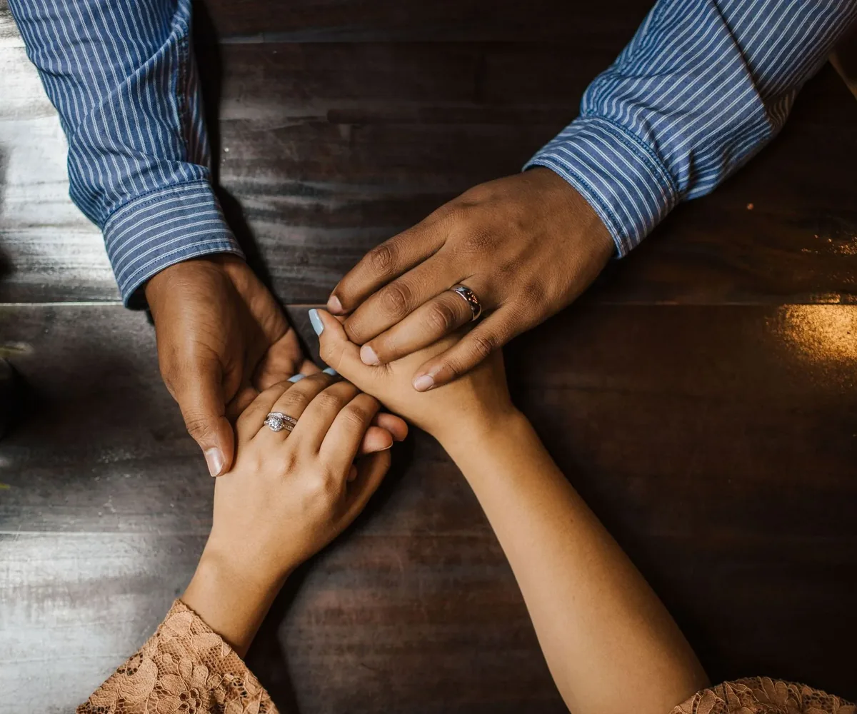 Manos de una pareja entrelazadas sobre una mesa de madera oscura