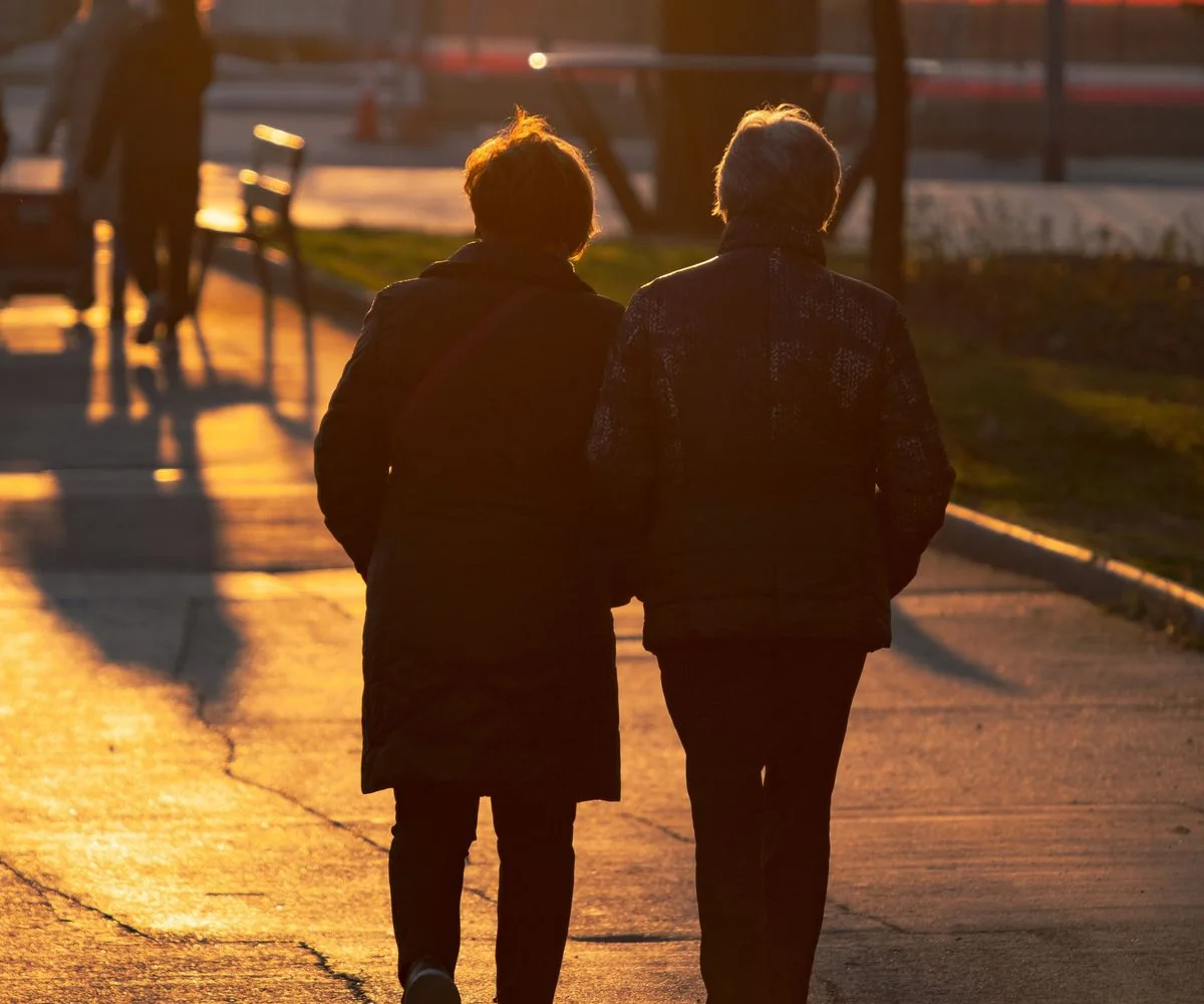 Pareja de adultos mayores caminando juntos por un parque, a contraluz en un atardecer dorado