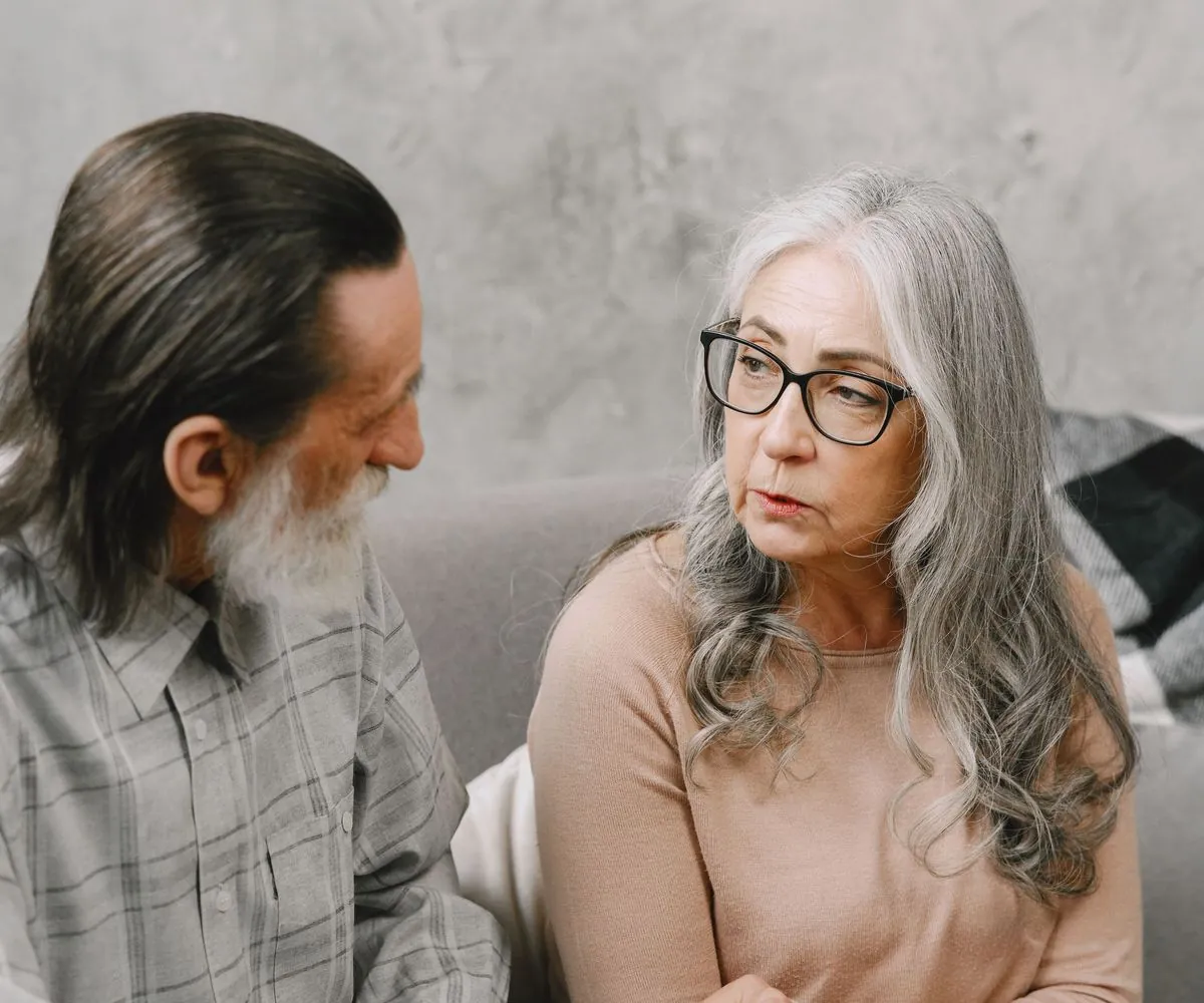 Pareja madura sentada en un sofá, conversando con calma y mirándose a los ojos