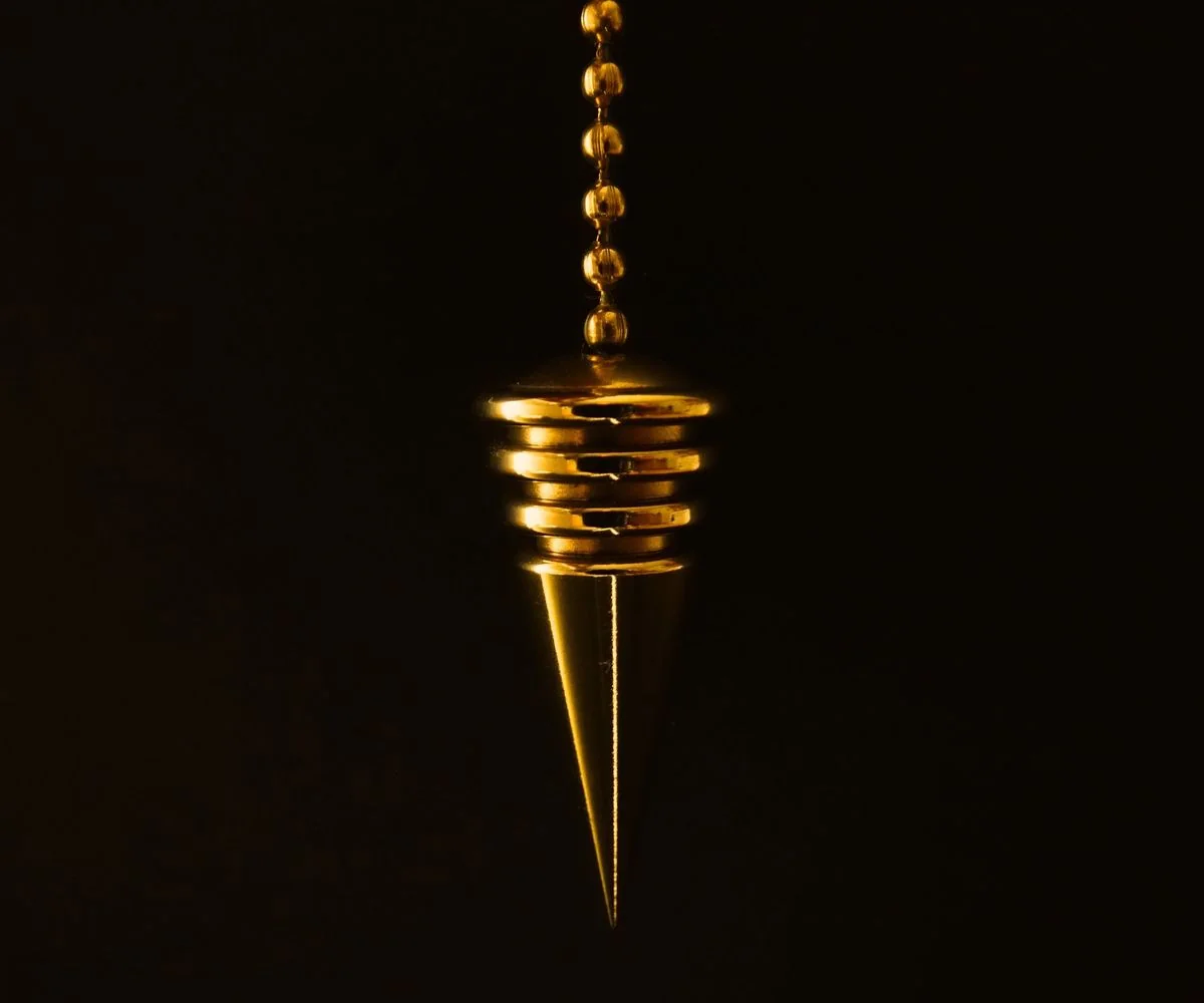 Péndulo dorado colgando de una cadena sobre fondo negro