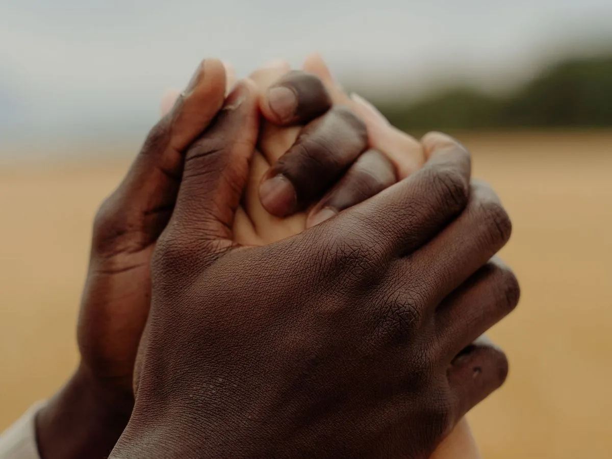 Dos manos que sostienen con fuerza la mano de otra persona, sobre un campo dorado