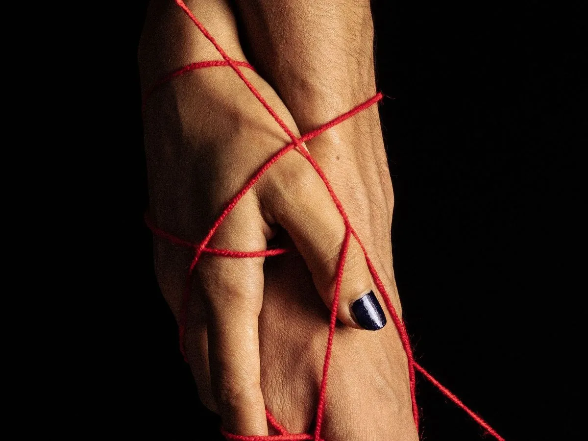 Dos manos entrelazadas y atadas con hilo rojo sobre un fondo oscuro