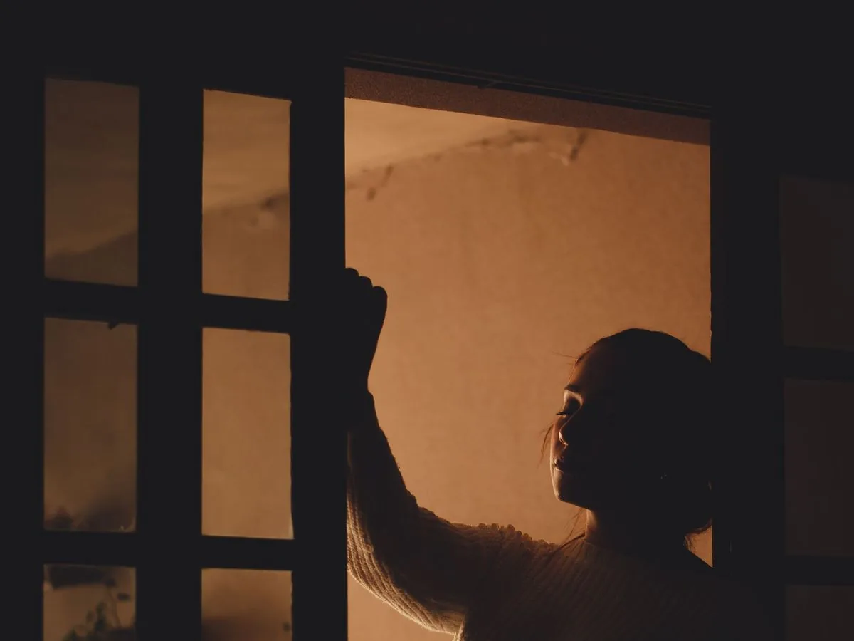 Silueta de una mujer que abre una ventana en una habitación en penumbra
