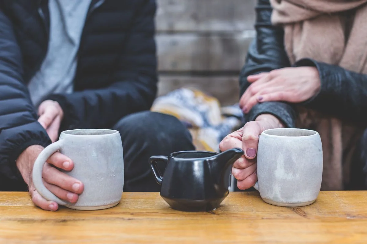 Manos de una pareja con tazas de café sobre una mesa de madera, en plena conversación