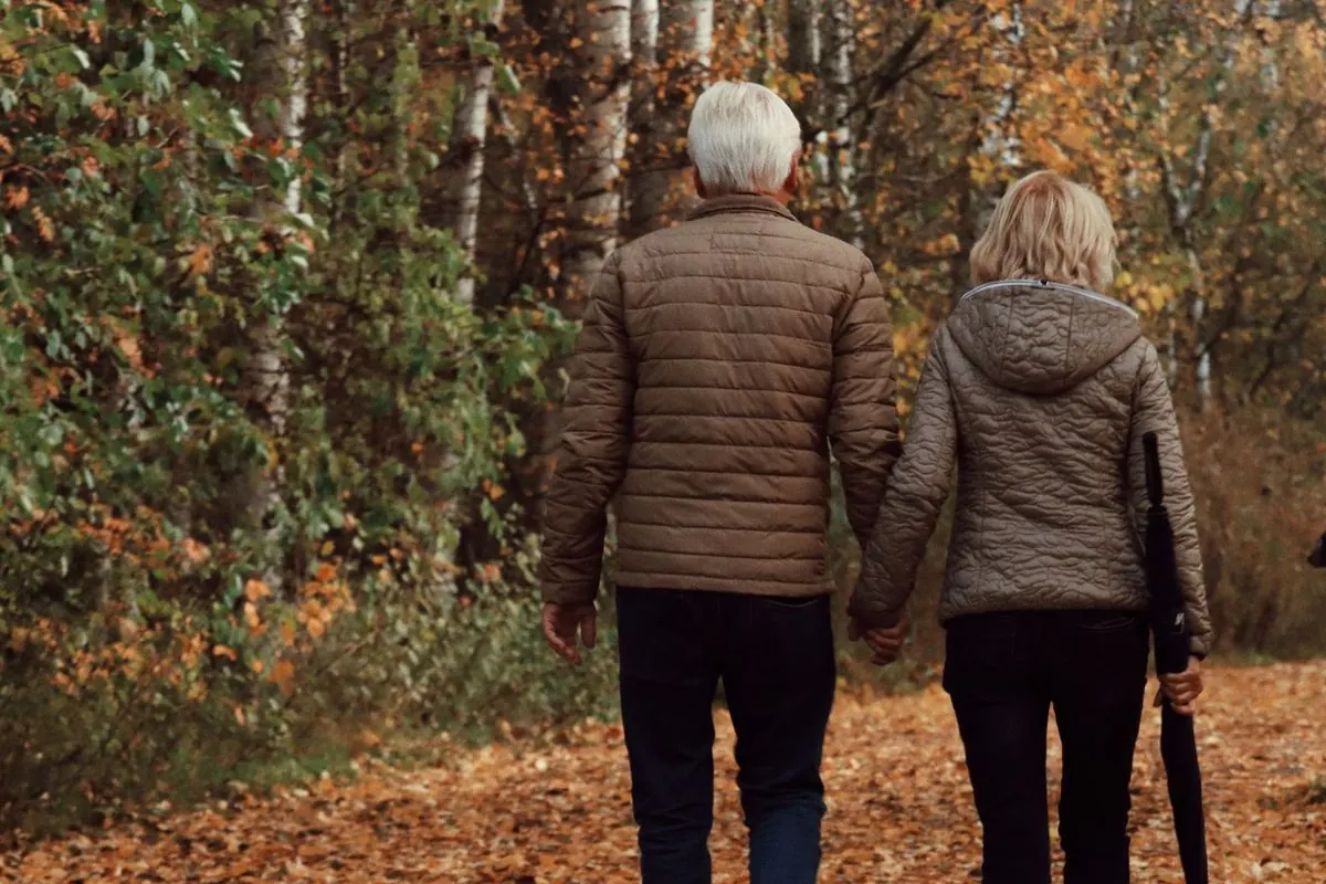 Pareja madura caminando de la mano por un sendero cubierto de hojas de otoño