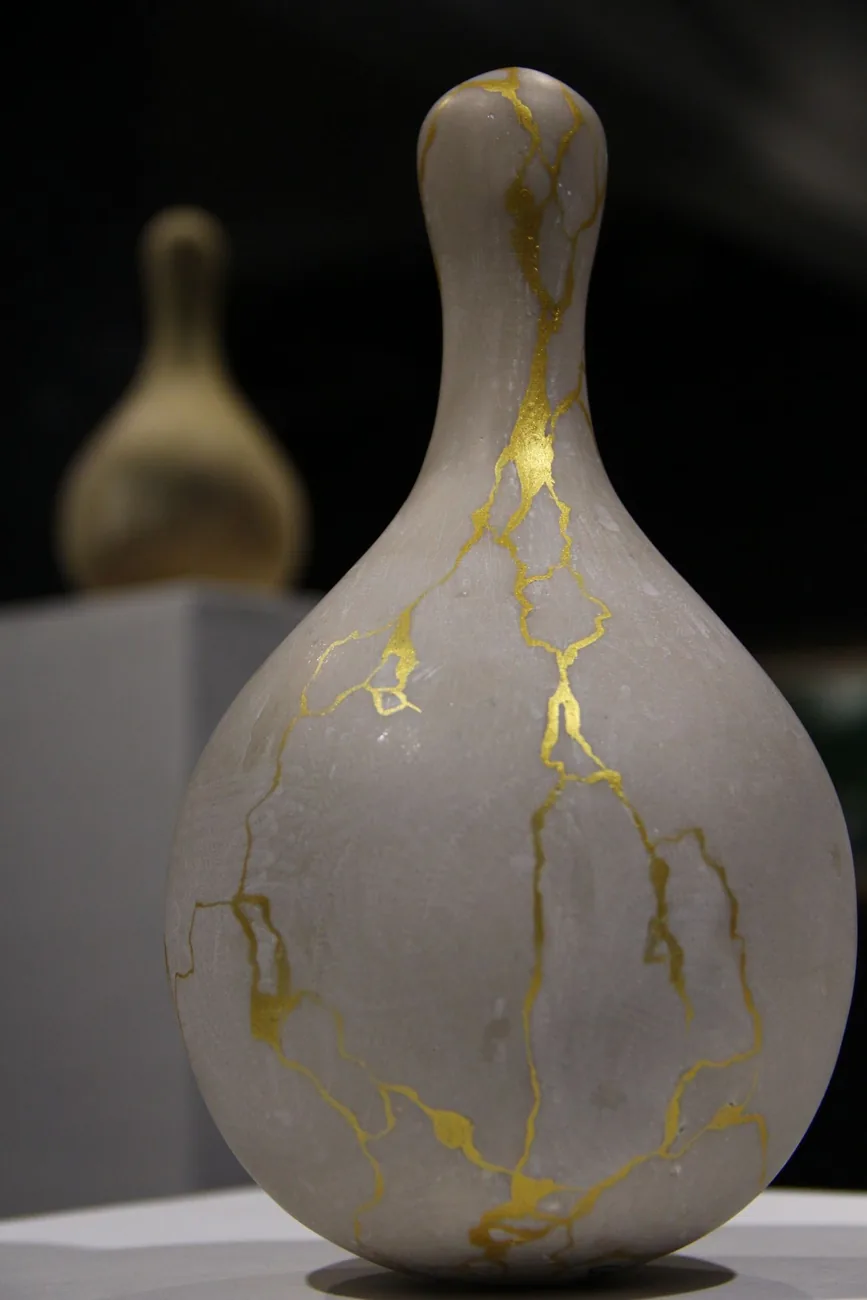 Vasija de cerámica reparada con kintsugi: grietas rellenas de oro sobre fondo oscuro