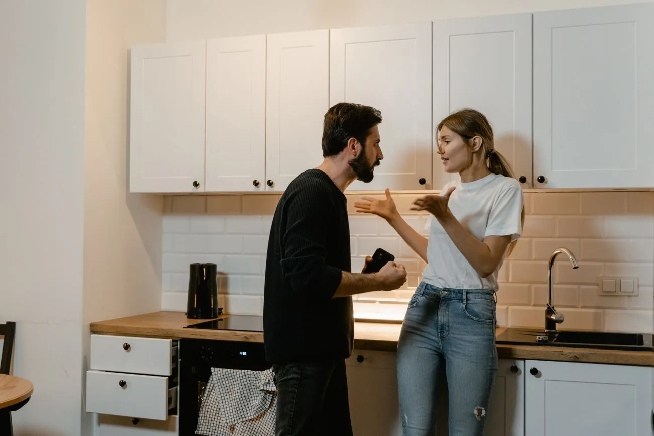 Pareja discutiendo de pie en una cocina de luz cálida, gesticulando con las manos