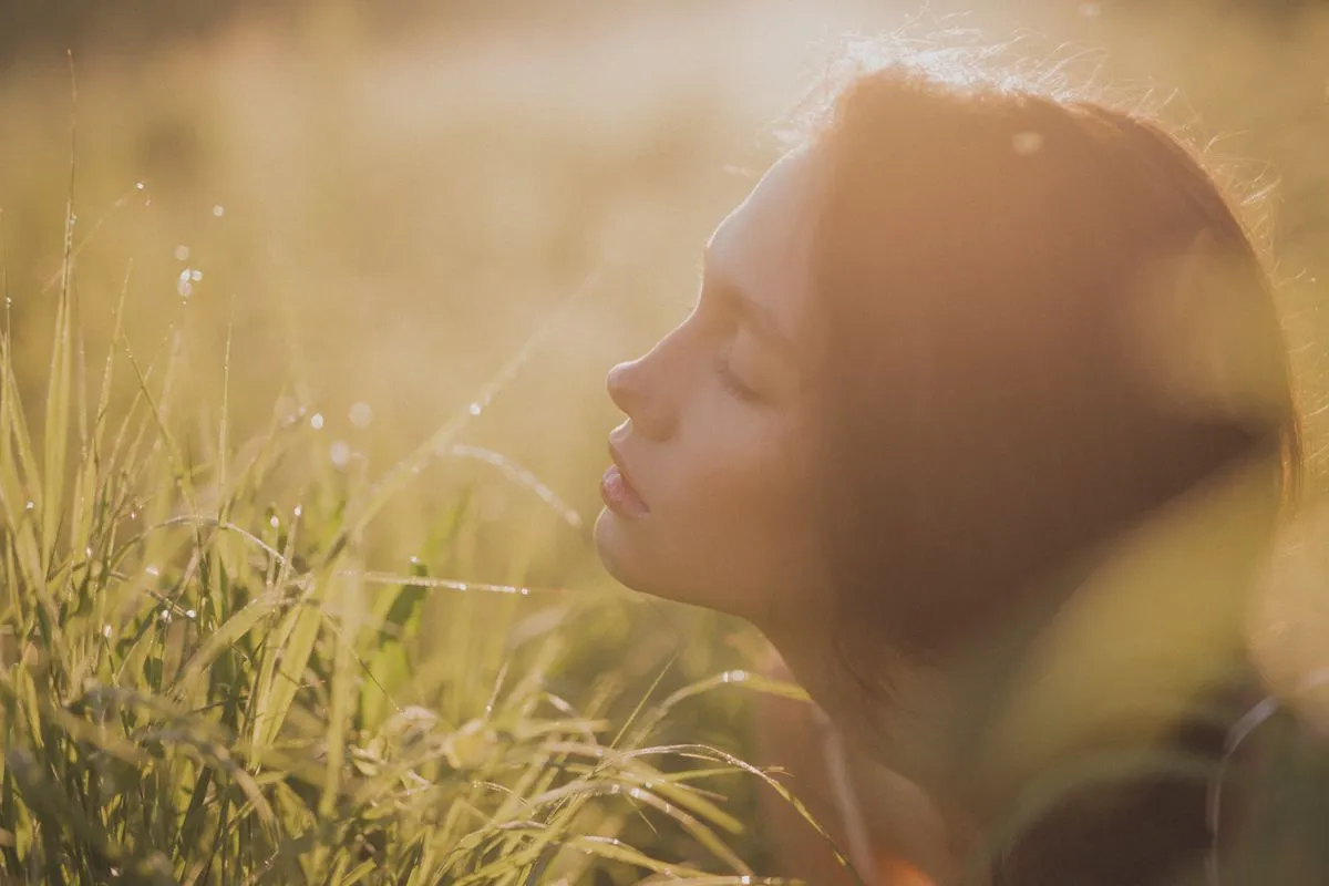 Mujer con los ojos cerrados entre pasto dorado, iluminada por el sol