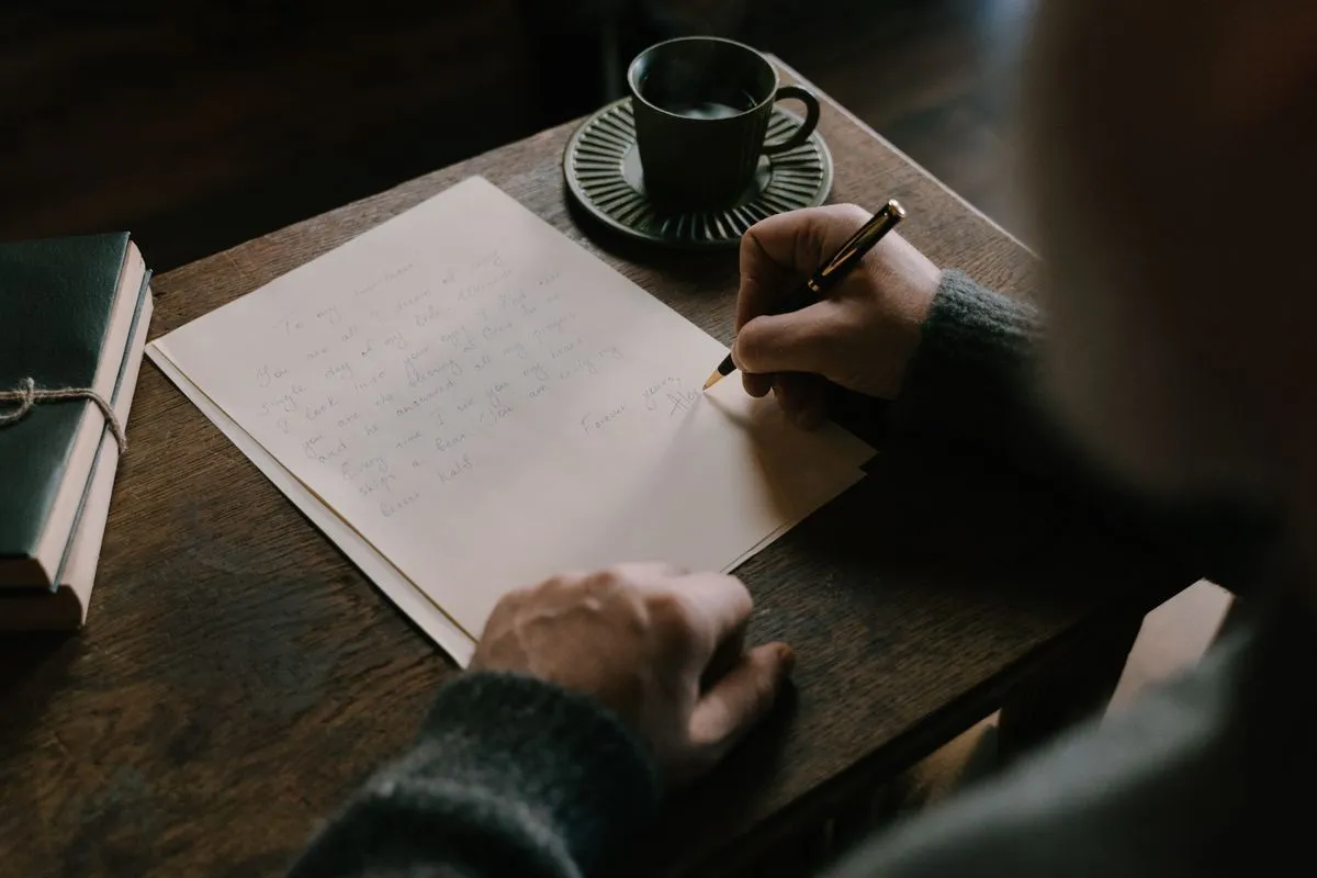 Manos escribiendo una carta a mano sobre un escritorio de madera