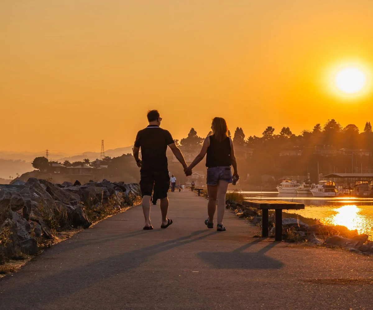 Pareja de espaldas caminando de la mano por un sendero junto al mar, al atardecer