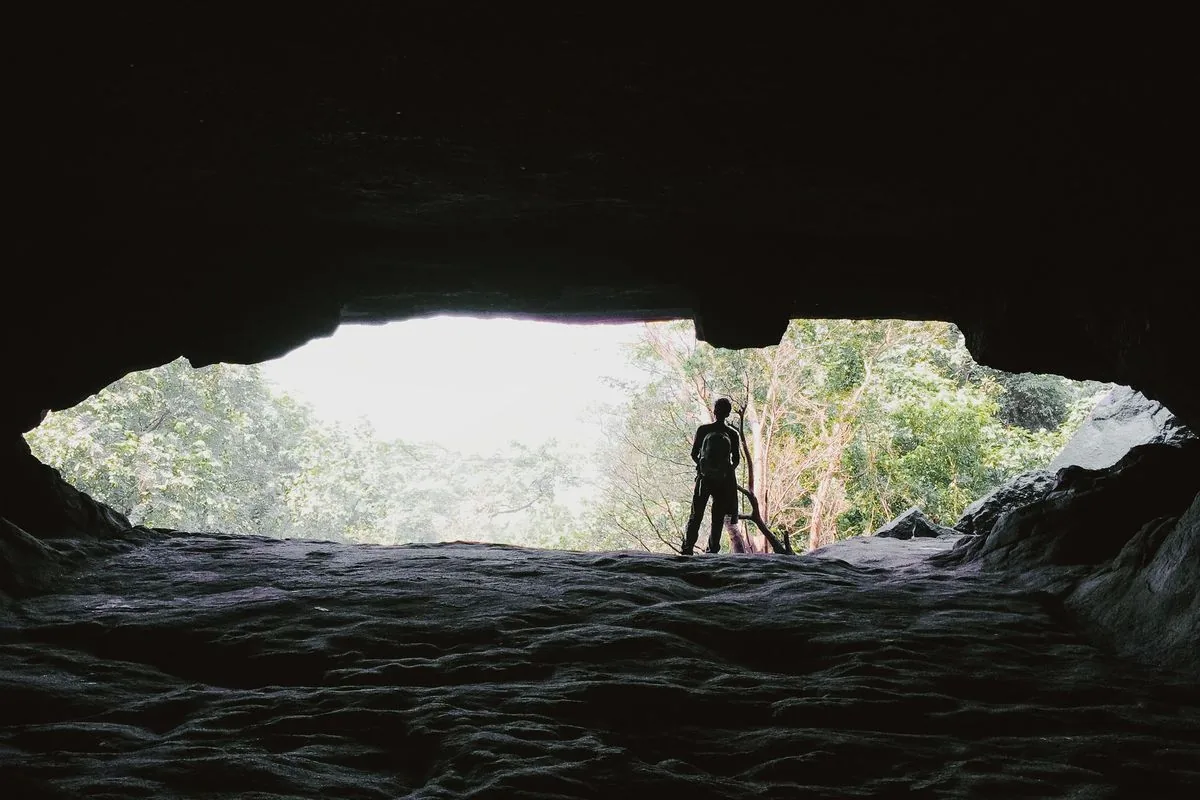 Silueta de un hombre de pie en la salida de una cueva oscura, frente a un bosque iluminado