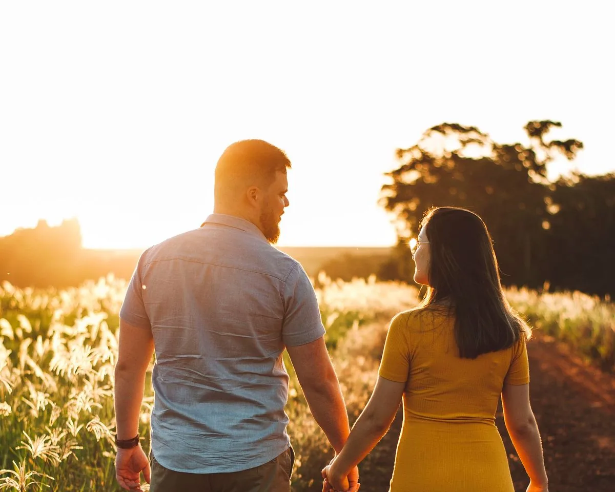Pareja de espaldas caminando de la mano por un sendero al atardecer