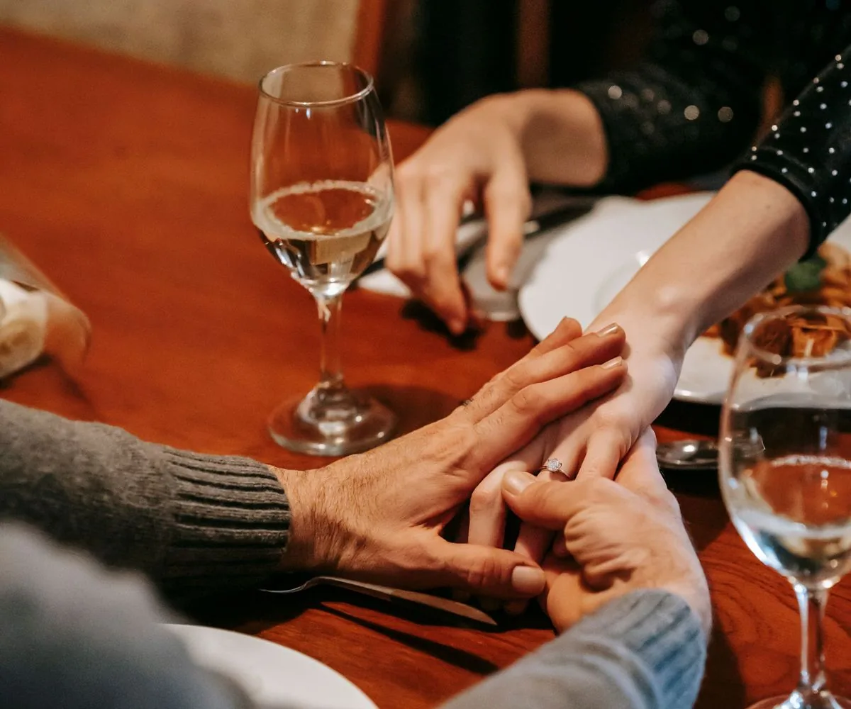 Manos de una pareja entrelazadas sobre la mesa durante una comida familiar