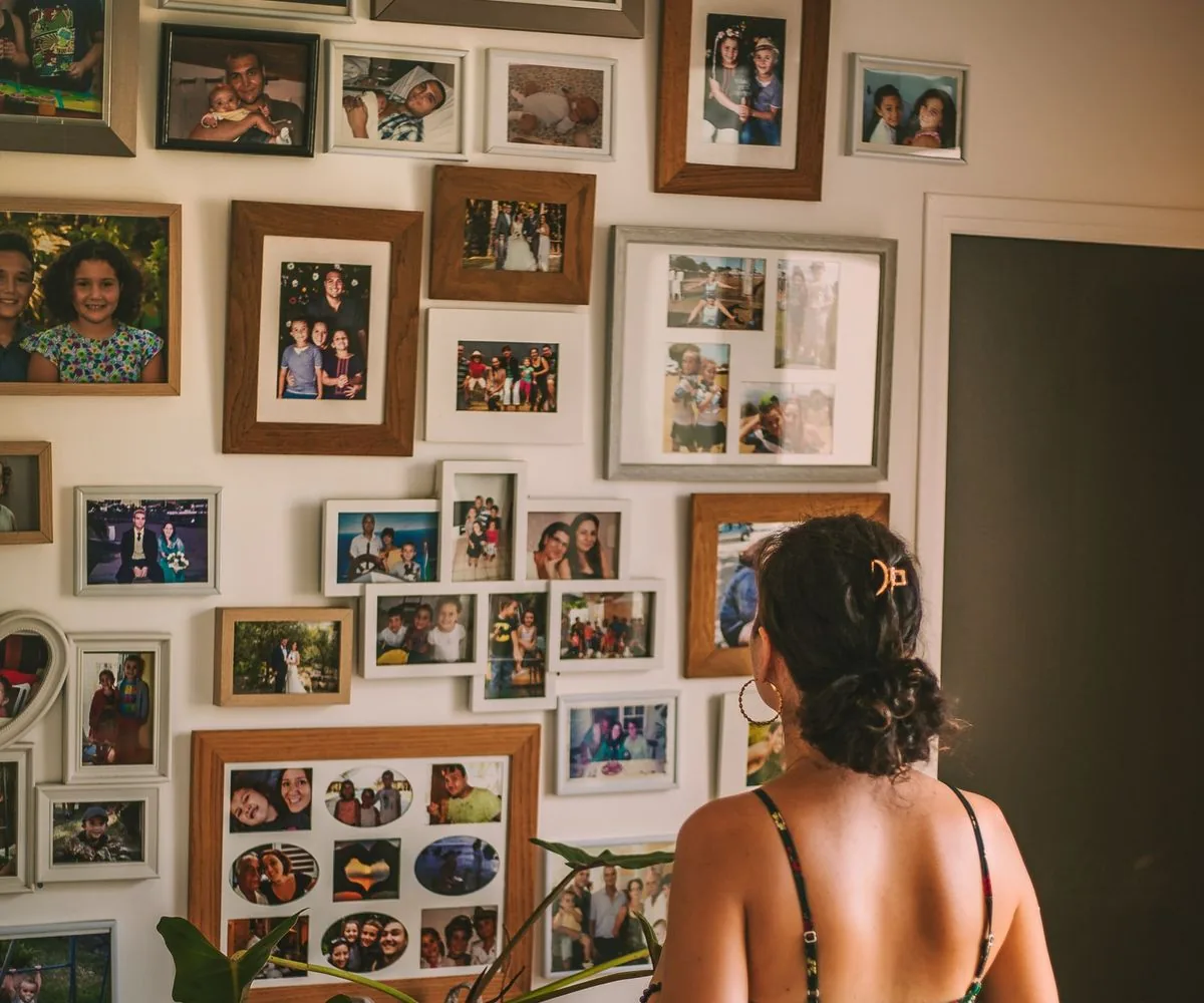 Mujer de espaldas mirando una pared llena de fotos familiares enmarcadas