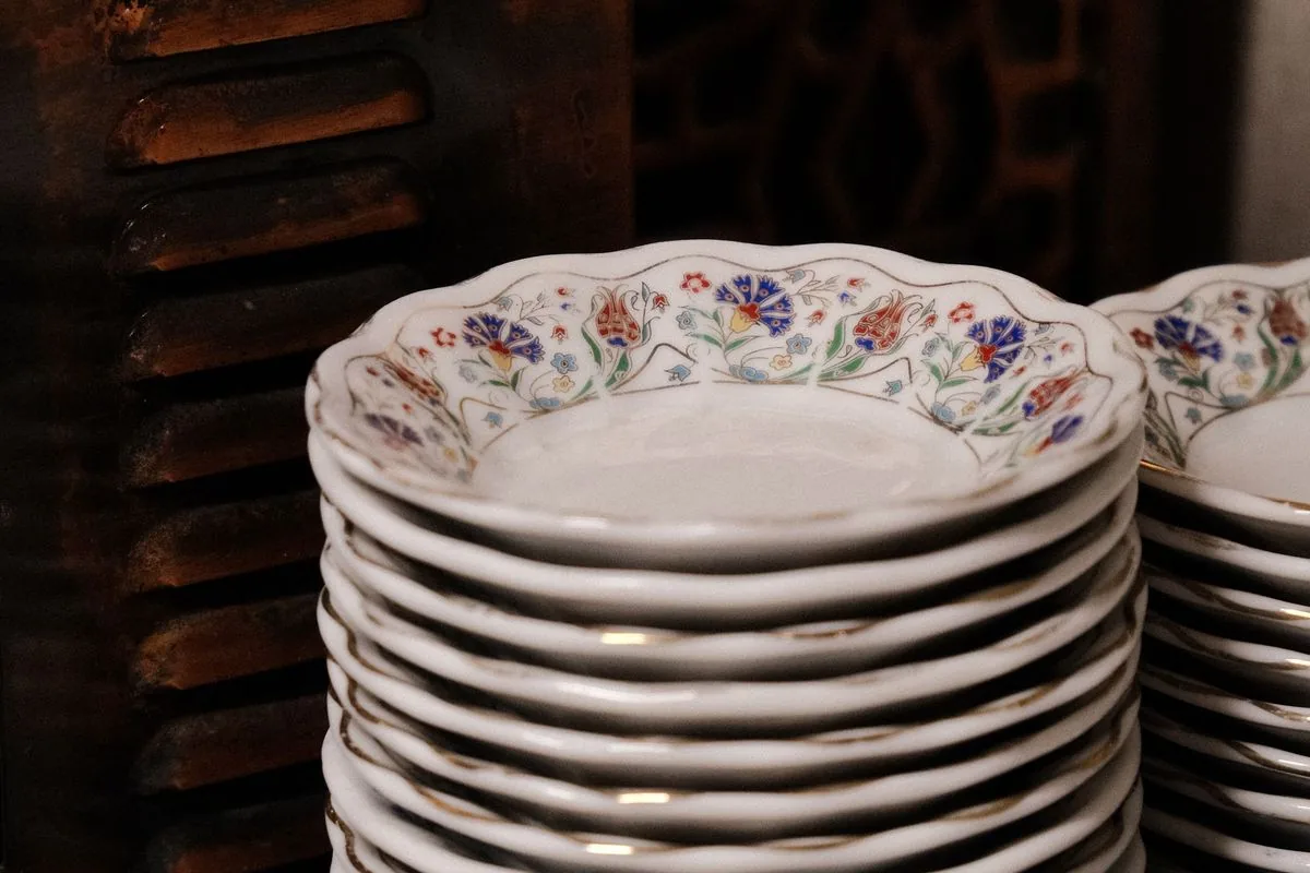 Platos de porcelana con bordes de flores pintadas, apilados frente a un mueble de madera oscura